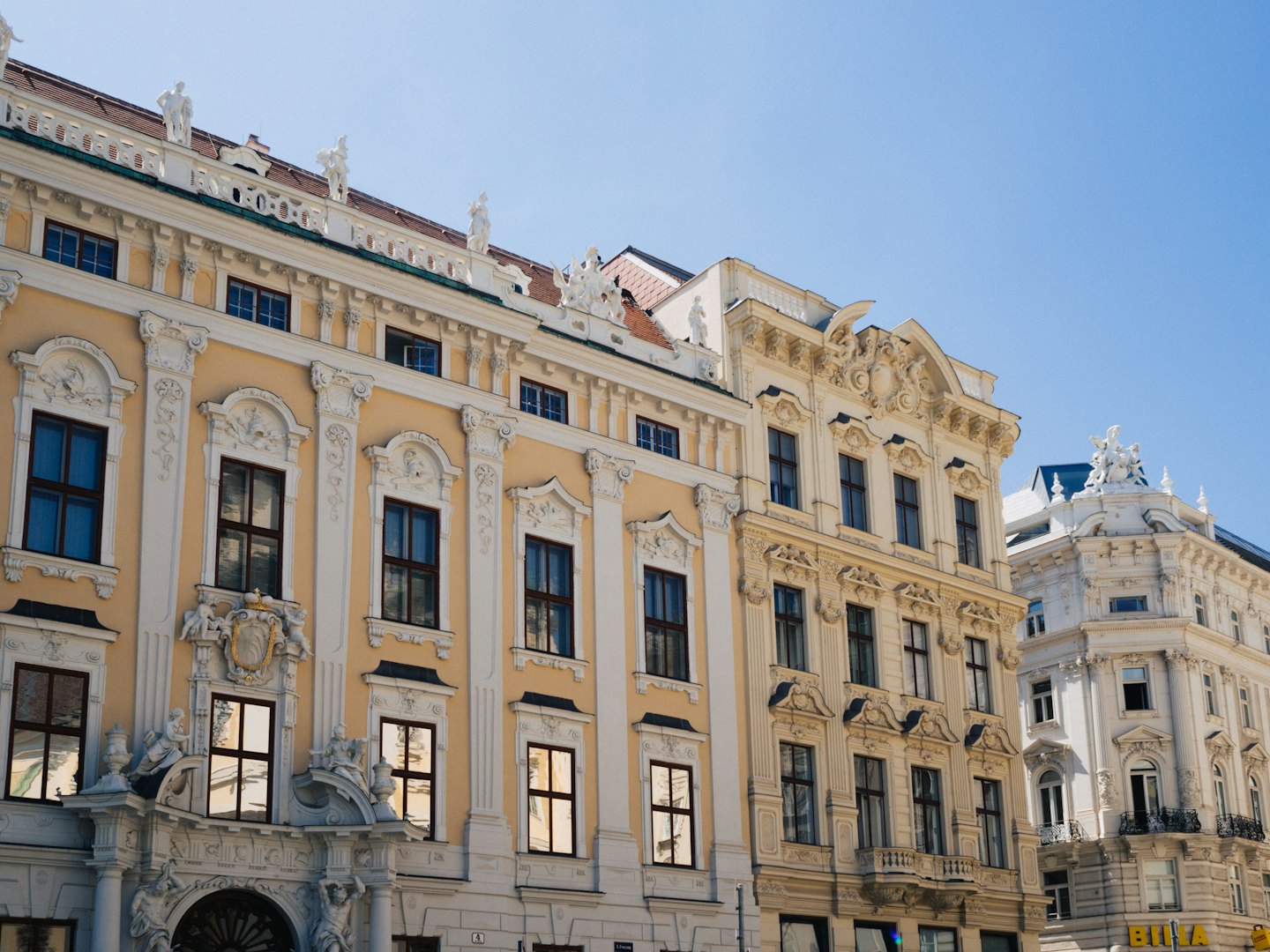 Ornate European Baroque buildings with decorative statues under a blue sky.