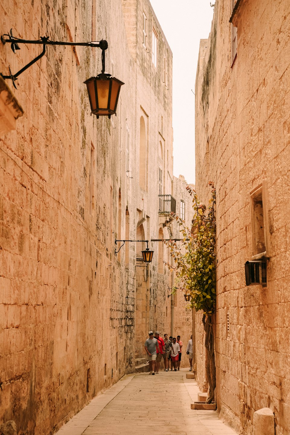 Tourists walk down a narrow stone alleyway lined with medieval buildings.