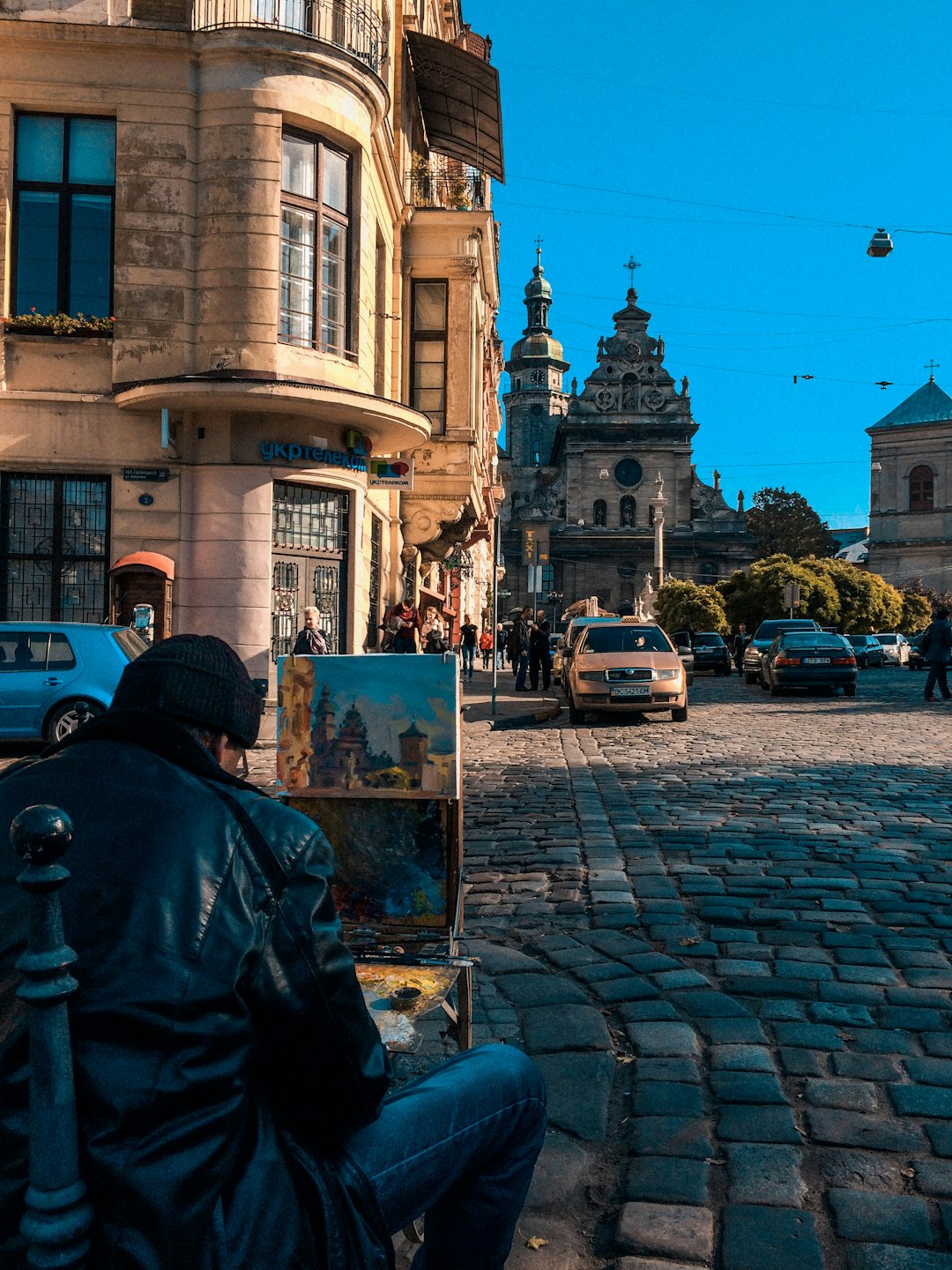 Artist painting a cityscape on an easel on a cobblestone street.