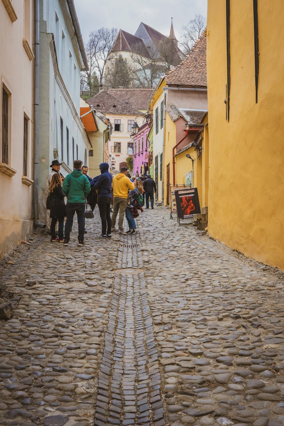 Tourists walk along a narrow cobblestone street in a historic town.